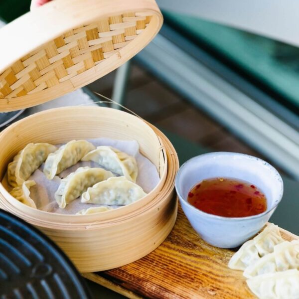 Dim sum cocinados al vapor en una canasta de bambú, acompañados de una salsa para dip.