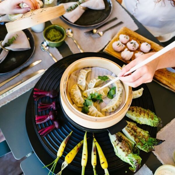 Dim sum al vapor servidos en canasta de bambú, con zanahorias asadas y lechuga sobre una parrilla.