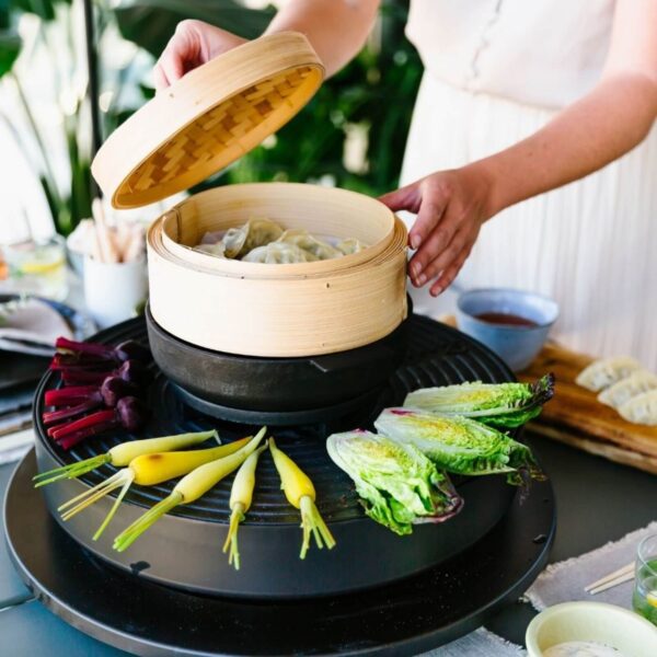 Canasta de bambú con dim sum cocinándose al vapor en parrilla, junto a zanahorias y lechugas asadas.