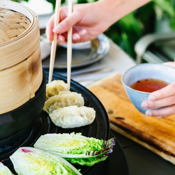 Persona usando palillos para tomar dim sum de una parrilla, con lechuga asada y salsa para dip.