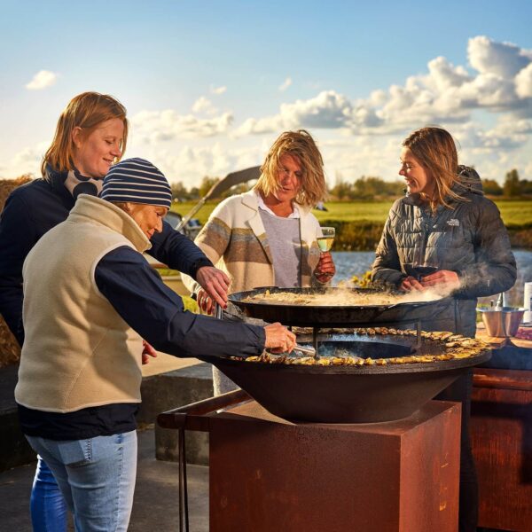 Grupo de personas cocinando en la parrilla Fuego Directo OFYR modelo 85 en un entorno al aire libre, disfrutando de la experiencia culinaria.