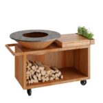 OFYR Island 100 PRO barbecue with corten steel finish, teak worktop, wood storage compartment and wheels for easy movement.