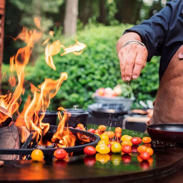 Persona sazonando tomates cherry en una barbacoa OFYR con Anillo Anticaída, evitando que los alimentos caigan al fuego.