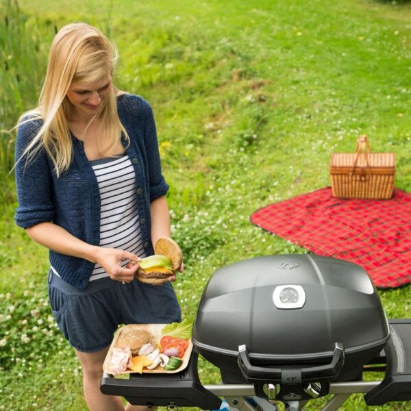 Mujer preparando una hamburguesa junto a la parrilla Napoleon TravelQ PRO285 en un picnic.