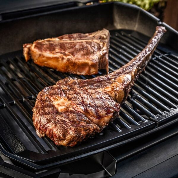 Tomahawk steak y T-bone steak cocinándose sobre las rejillas de una Barbacoa Weber PULSE 2000.