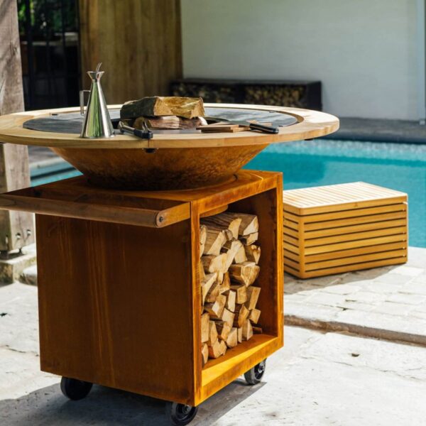 Barbacoa OFYR con Anillo de Protección Contra Quemaduras de madera de teca y almacenamiento de leña junto a una piscina.