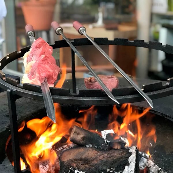 Brochetas de acero inoxidable con carne asándose sobre una parrilla al fuego, ideal para asados al aire libre.