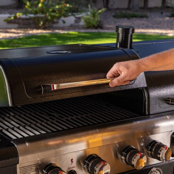 Persona abriendo la tapa de la barbacoa Pit Boss Memphis V2, mostrando las parrillas de cocción y los controles de temperatura en un entorno al aire libre.