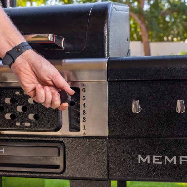 Mano ajustando la altura de la bandeja de carbón en la barbacoa Pit Boss Memphis V2 mediante su sistema de regulación de seis niveles.