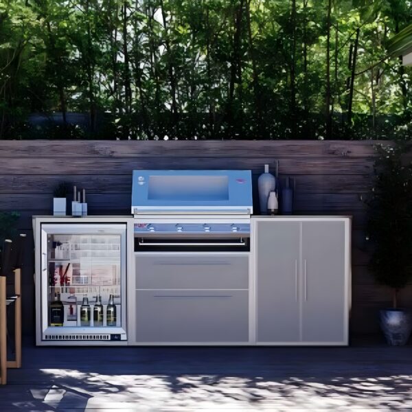 Cocina de exterior con nevera Beefeater de acero inoxidable y puerta de cristal junto a una parrilla integrada, rodeada de naturaleza.