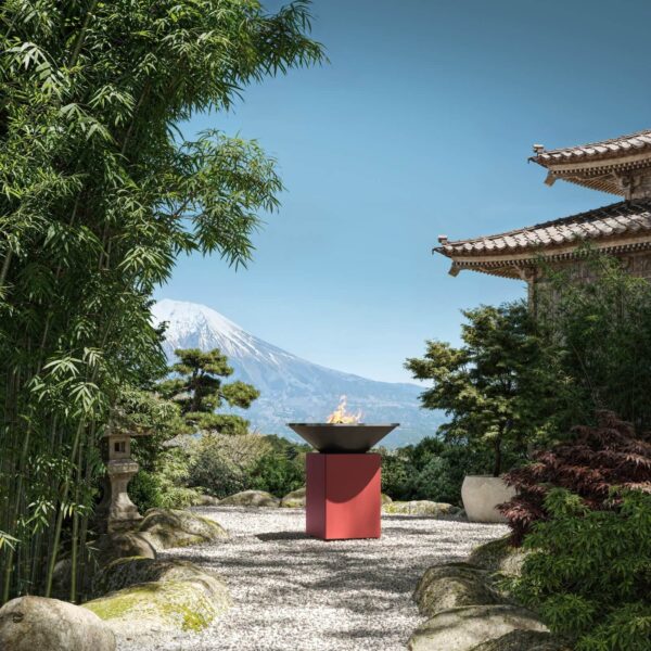 Barbacoa OFYR Oxide Red con fuego encendido en un jardín japonés, con bambú, un templo tradicional y el monte Fuji al fondo.