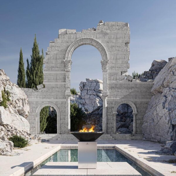 Barbacoa OFYR de acero inoxidable cepillado con fuego encendido, situada en un entorno monumental con ruinas de piedra y una piscina reflectante.