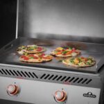 Plancha encastrable de acero inoxidable Serie 700 cocinando pizzas gourmet con vegetales frescos sobre superficie caliente.
