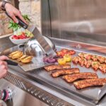 Plancha encastrable de 32 pulgadas en uso con verduras, camarones, carne y espátulas sobre superficie de acero inoxidable caliente.