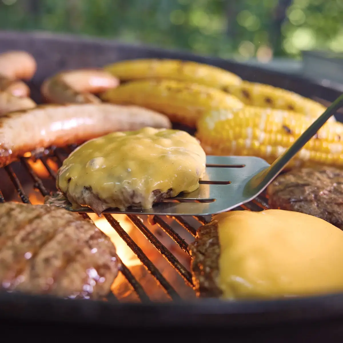 Hamburguesas, salchichas y mazorca cocinándose en una barbacoa de carbón Weber