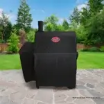 Funda Char-Griller 5533 sobre una parrilla en un patio de piedra con jardín verde en configuración compacta.