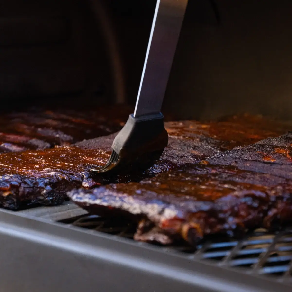 Brocha Char-Griller aplicando salsa sobre costillas en la parrilla
