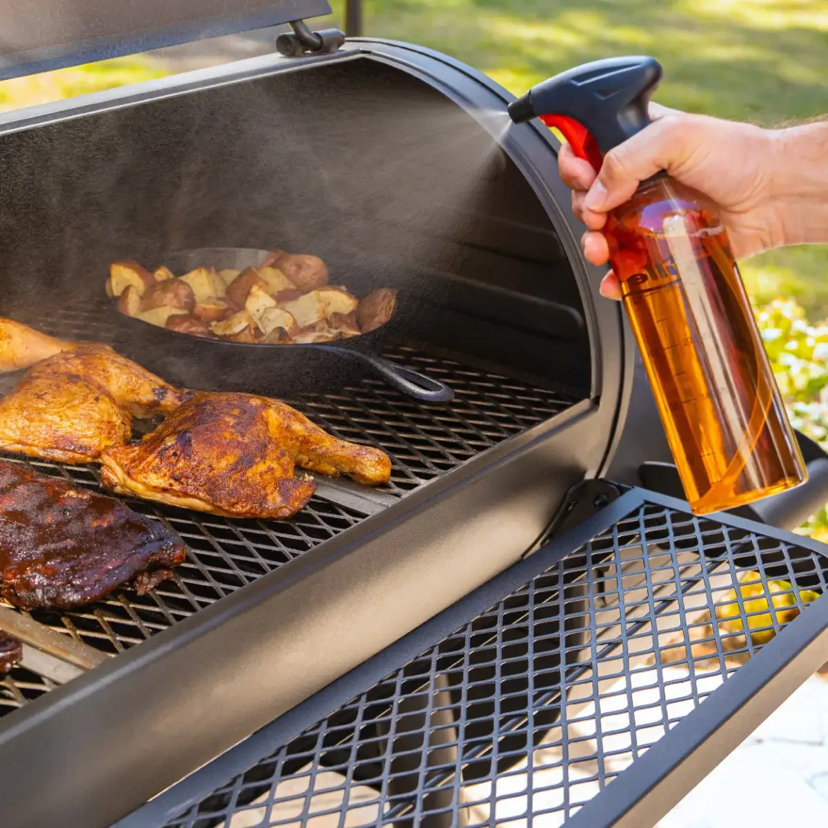 Botella pulverizadora Char-Griller utilizada junto a pollo y patatas en la barbacoa