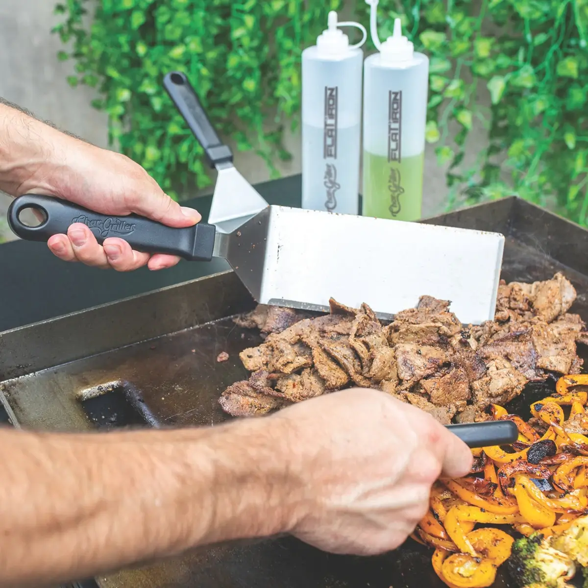 Dos espátulas Char-Griller moviendo carne y pimientos sobre una plancha