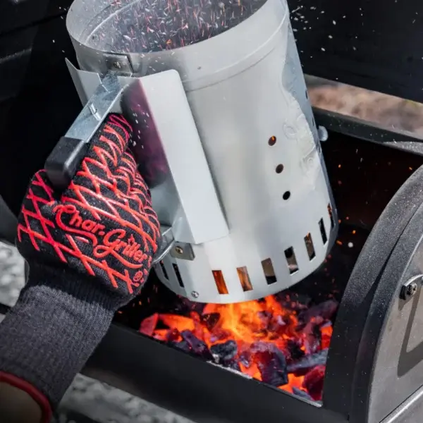 Mano con guante térmico usando el gatillo del encendedor de chimenea Char-Griller para soltar carbón caliente dentro de una parrilla.