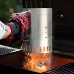 Guante térmico accionando el encendedor de chimenea Char-Griller mientras caen chispas y carbón caliente dentro de la parrilla.