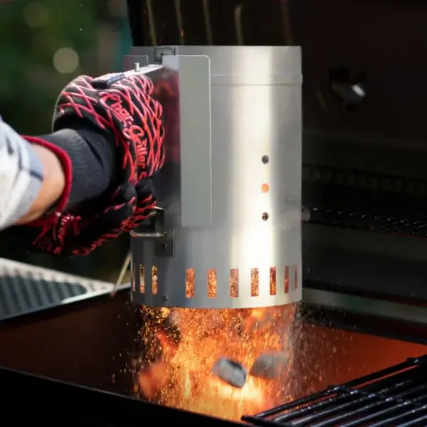Guante térmico accionando el encendedor de chimenea Char-Griller mientras caen chispas y carbón caliente dentro de la parrilla.