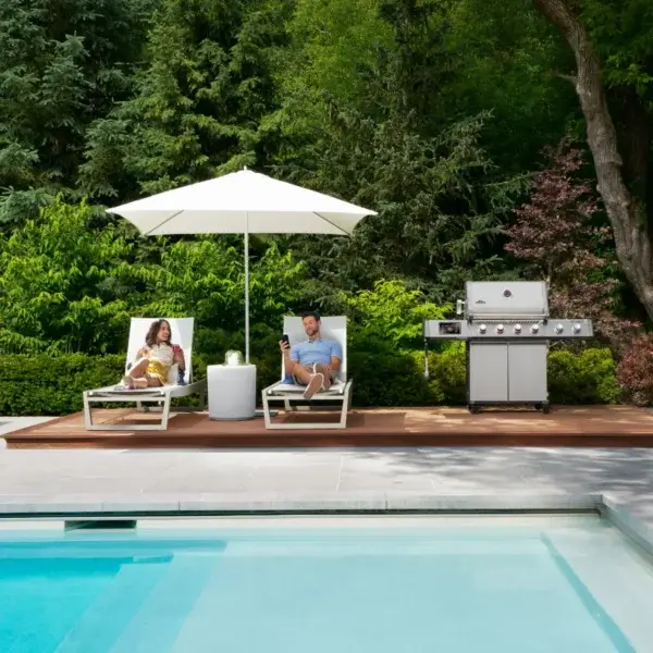 Parrilla Napoleon Prestige PRO 500 VX en un exterior junto a piscina con personas y zona de comida