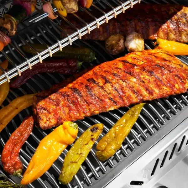 Primer plano de la parrilla Napoleon Prestige PRO 665 Elite en uso con costillas, brochetas y verduras asándose
