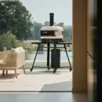 Gozney Dome Gen 2.0 Bone sobre soporte con ruedas en una terraza con vistas al agua.