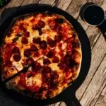 Pizza de pepperoni en una sartén negra sobre una mesa de madera, vista desde arriba.