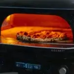 Pizza horneándose dentro del Gozney Dome Gen 2.0 con llama y panel digital visibles.