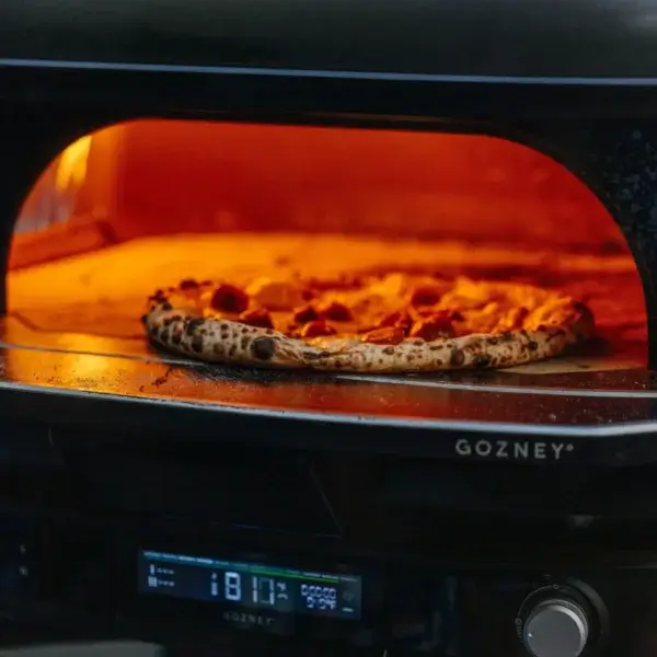Pizza horneándose dentro del Gozney Dome Gen 2.0 con llama y panel digital visibles.