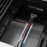 Quemador tubular de la GrandPro Maxim G5 encendido con llama azul bajo la zona de cocción.