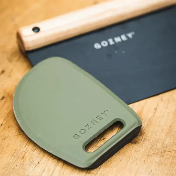 Raspador Gozney Dough Scraper verde sobre una mesa de madera junto a un cortador de masa Gozney.