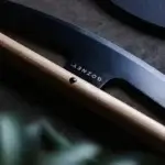 Detalle del Gozney Pizza Rocker con logotipo sobre la cuchilla negra, filo metálico y mango de madera sobre una superficie oscura.