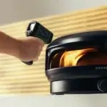 Mano utilizando el termómetro infrarrojo Gozney para medir la temperatura de un horno de pizza Gozney encendido.