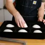 Persona con delantal manipulando una bola de masa dentro de una Gozney Dough Tray abierta.