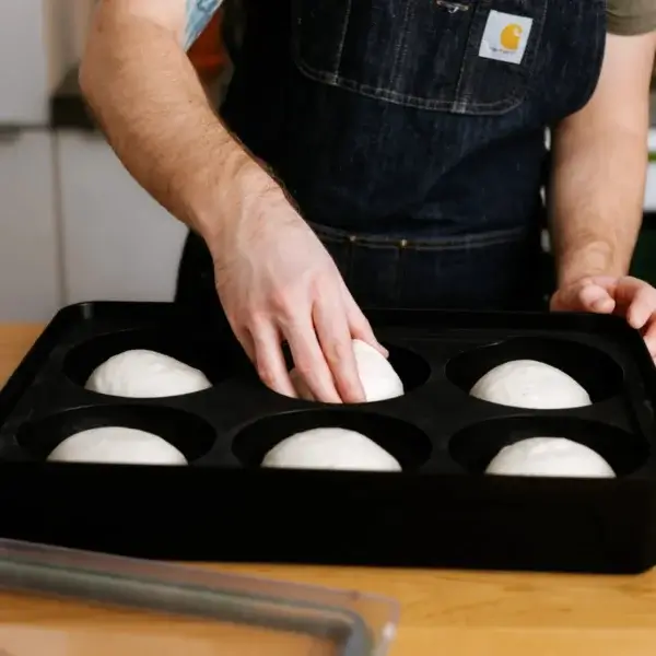 Persona con delantal manipulando una bola de masa dentro de una Gozney Dough Tray abierta.