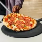 Pizza de pepperoni sobre una Gozney Pizza Server de 18 pulgadas mientras una persona la corta