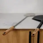 Pala Gozney Utility apoyada sobre una encimera junto a otro accesorio Gozney con mango de madera.