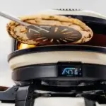 Pala perforada Gozney Balance levantando una pizza en un horno Gozney con llama y pantalla digital visibles.
