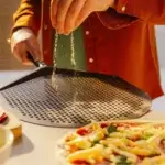 Persona espolvoreando harina sobre una pala Gozney Pro Peel junto a una pizza preparada.