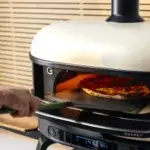 Mano sujetando una Gozney Pro Peel 16 XL para introducir una pizza en un horno Gozney encendido.