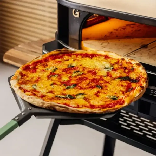 Pizza cocinada sobre una pala Gozney Pro Peel 16 XL frente a la boca de un horno Gozney.