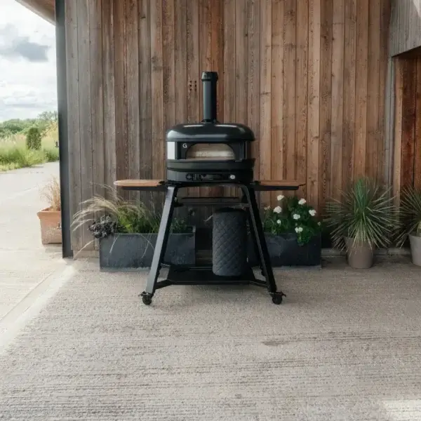 Soporte Gozney Dome Gen 2 con horno Off-Black en una terraza exterior junto a una pared de madera y maceteros.