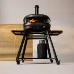 Soporte Gozney Dome Gen 2 con horno Off-Black encendido, visto de frente, alas laterales de madera y bombona cubierta en la balda inferior.