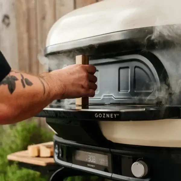 Mano colocando la puerta Gozney Dome Gen 2 en un horno exterior con vapor.