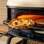 Pizza on a peel at the opening of the Gozney Dome Gen 2.0 oven, using the front shelf as a landing space.