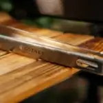Detalle del logotipo Gozney grabado en las pinzas de fuego vivo sobre una tabla de madera.