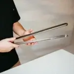 Persona sosteniendo las pinzas Gozney sobre fondo neutro.